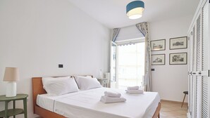 Een net opgemaakt bed met witte lakens en handdoeken, een bedlampje en een klein nachtkastje in groen.