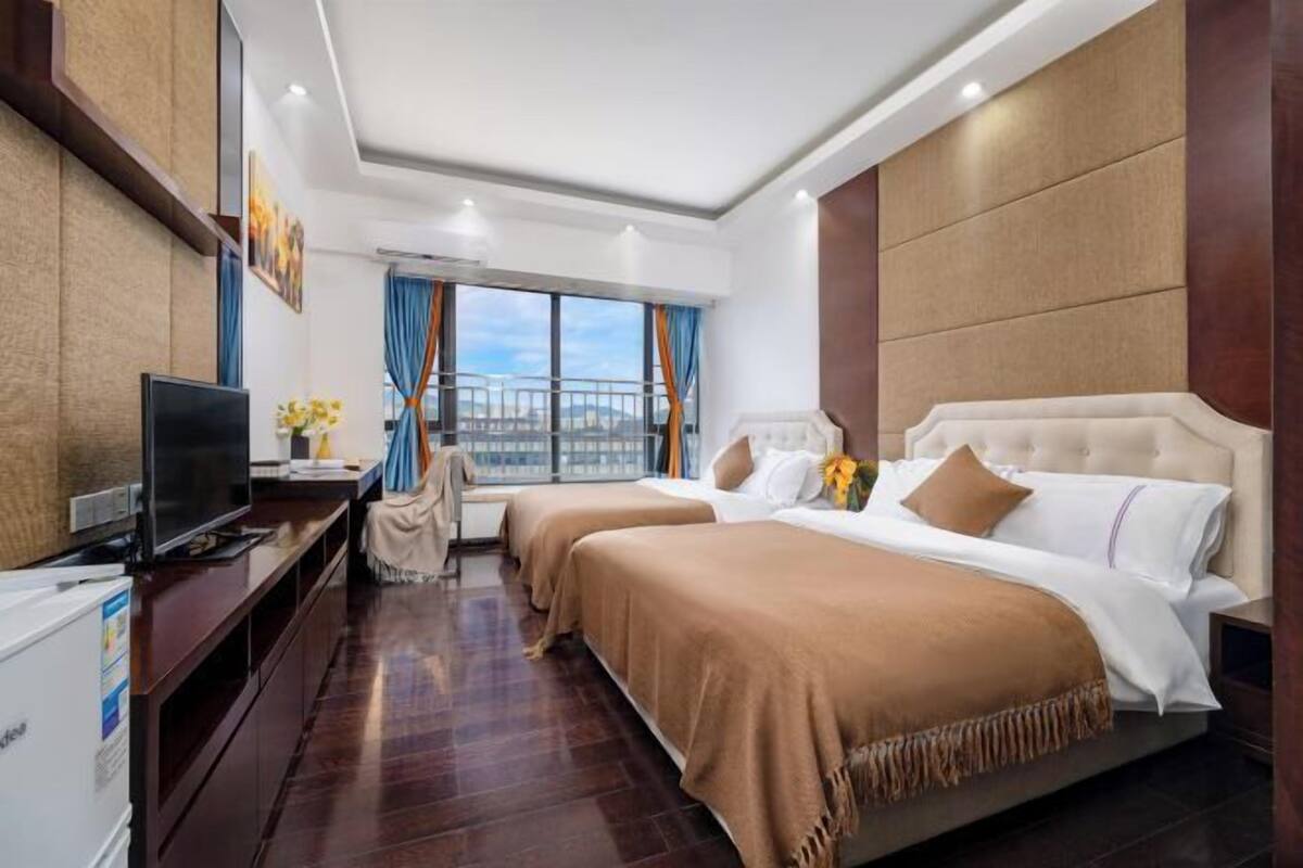 A hotel room with two beds, a TV, a desk, and a view of the city.