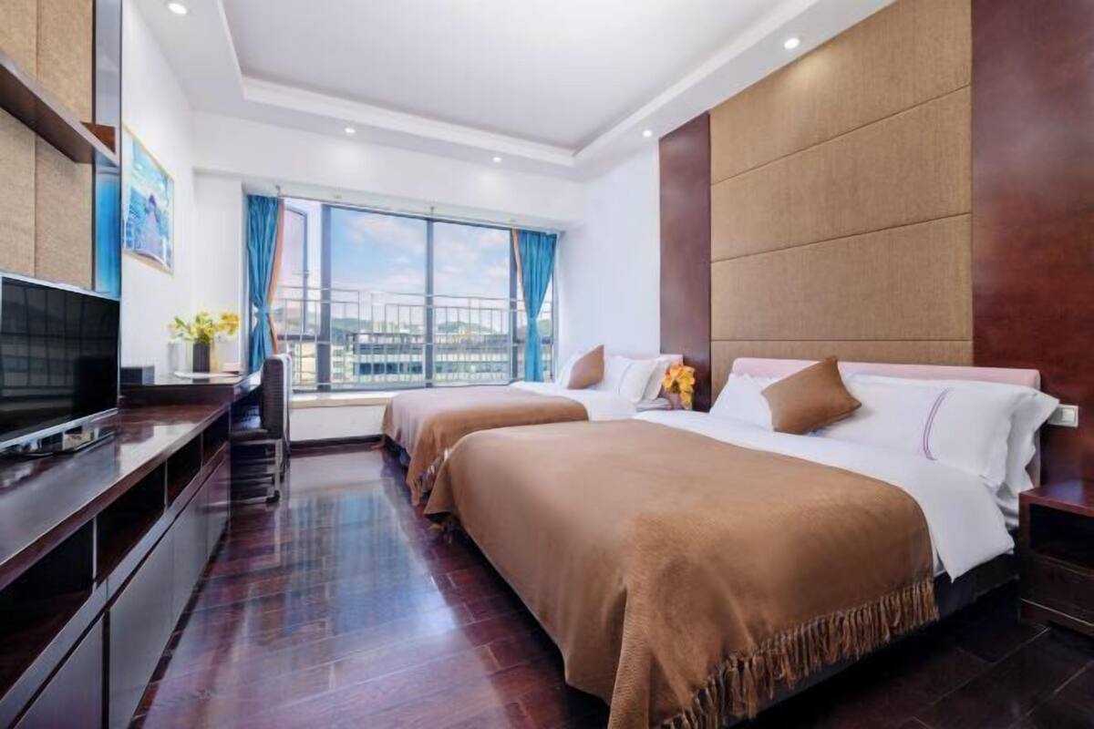 A hotel room with two beds, a TV, a desk, and a large window with a view.