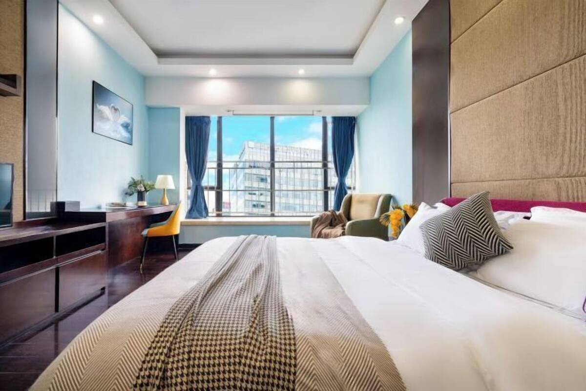 A modern hotel room with a large bed, a desk, and a window with a city view.