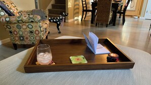A wooden tray with a glass of iced drink, a card, and a watch on a textured rug. - NW Crossing Getaway with all the amenities (Bend)