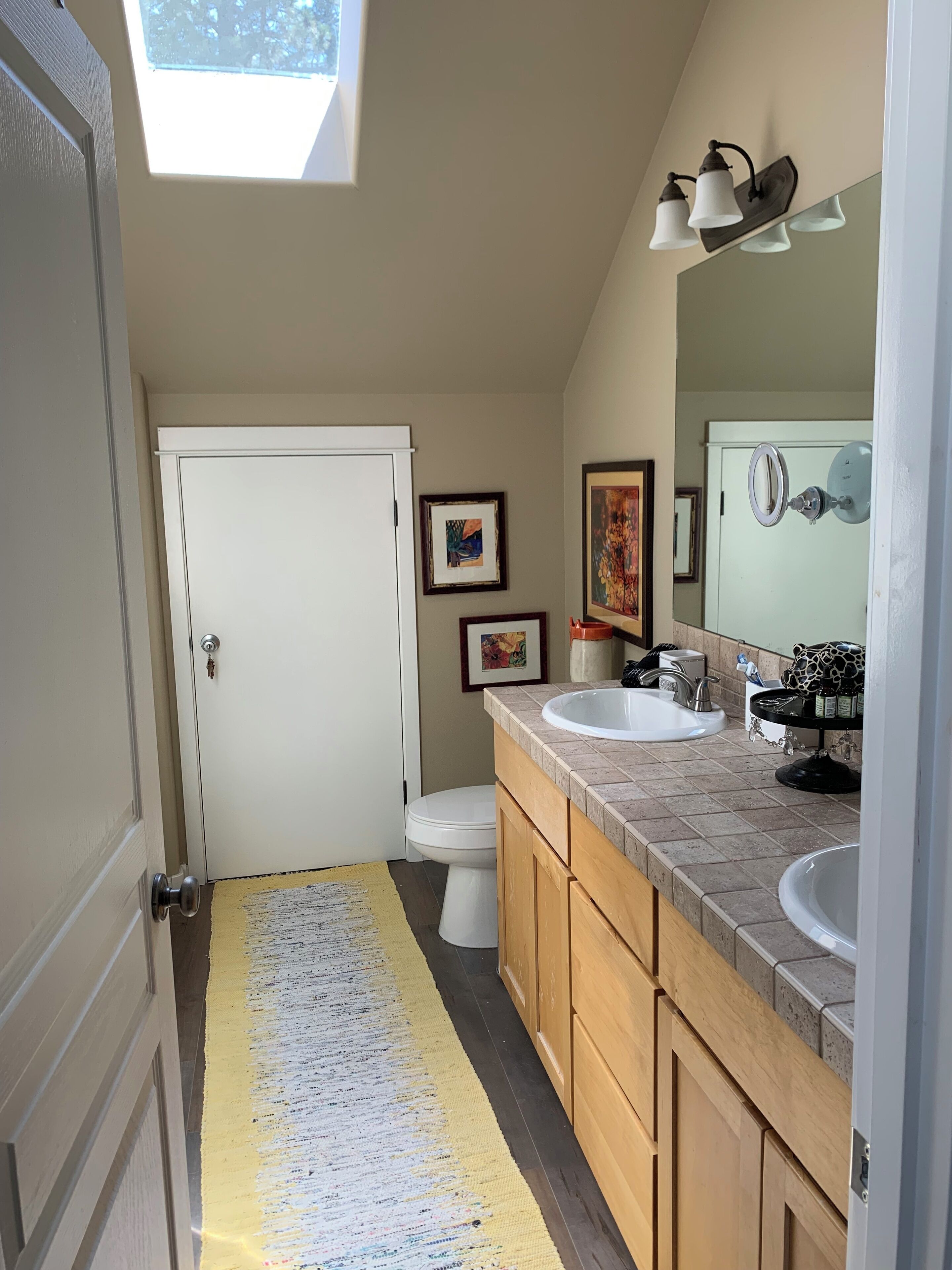 A compact bathroom with a skylight, a white toilet, a sink, and wooden cabinets.