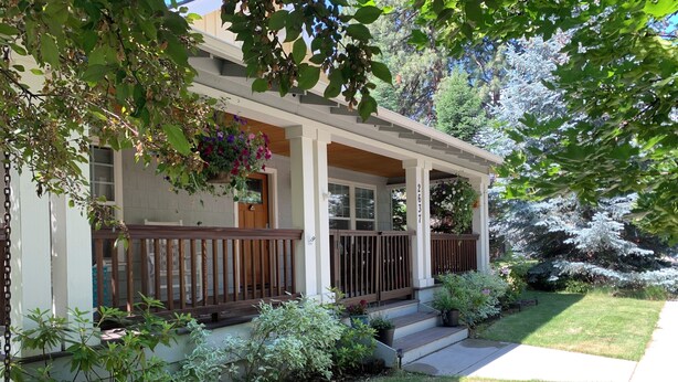 A two-story house with a covered porch, a well-maintained lawn, and a variety of potted plants. - NW Crossing Getaway with all the amenities (Bend)