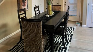 A dining area with a black and white striped rug, a wooden dining table, wicker chairs, a vase with flowers, and a hanging light fixture. - NW Crossing Getaway with all the amenities (Bend)