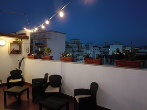 Una terraza en la azotea con plantas en macetas, luces colgantes y mobiliario de mimbre.