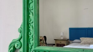 A room with a large green ornate mirror, a bed with a blue headboard, a nightstand with a lamp, and a chair. - Mille Lire B&B  (Palermo)