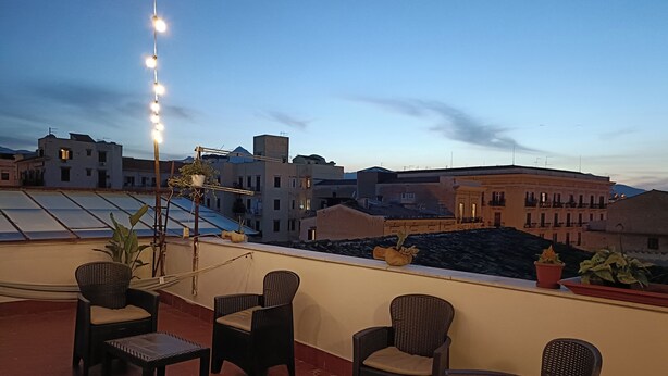 A rooftop terrace with wicker furniture, potted plants, and string lights. - Mille Lire B&B  (Palermo)