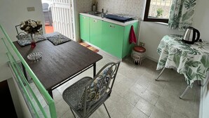 A compact kitchen with green cabinets, a dining table with chairs, a small window with curtains, and a clock on the wall. - Mille Lire B&B  (Palermo)
