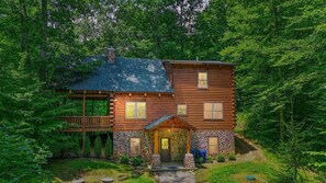 A log cabin with a stone foundation, a wooden deck, and a stone pathway leading to the entrance.