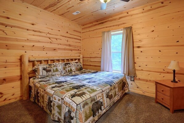 Ein Schlafzimmer einer Holzhütte mit einem Bett, einem Nachttisch und einem Fenster mit Vorhängen.