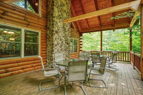 A covered outdoor area with a stone wall, wooden deck, and metal furniture. - Twin Creeks | Hocking Hills (Logan)