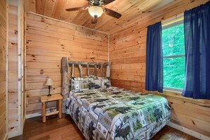 A wooden cabin bedroom with a bed, a nightstand, a lamp, and a window with curtains.