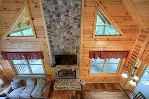A cozy cabin interior with a stone fireplace, wooden walls, and a sofa. - Twin Creeks | Hocking Hills (Logan)