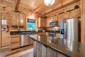 A wooden cabin-style kitchen with granite countertops, stainless steel appliances, and a window with a view of greenery.