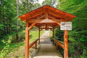 A wooden covered walkway leading to a lodge named 'Twin Creeks Lodge' under a large tree canopy.