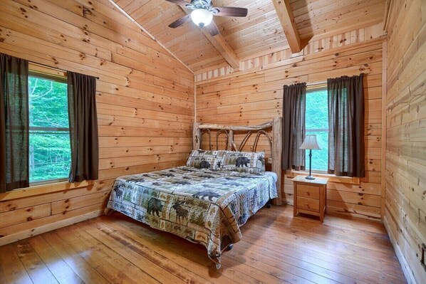 A wooden cabin bedroom with a bed, a nightstand, and a ceiling fan.