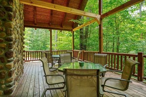 Eine überdachte Terrasse im Freien mit Steinwand, Holzgeländer und einer Sitzecke mit Tischen und Stühlen.