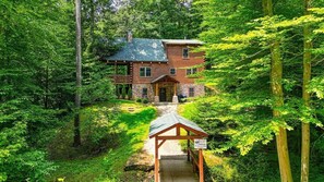 A log cabin with a stone foundation, surrounded by dense forest.