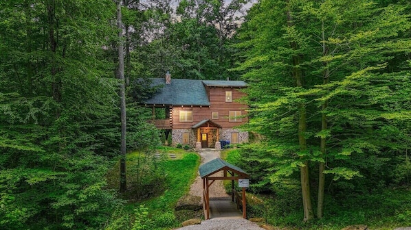 A log cabin with a stone foundation, surrounded by dense forest.