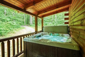 A wooden cabin with a hot tub and a view of a forested area.