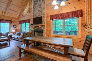 A wooden cabin interior with a stone fireplace, a dining table, and a sofa. - Twin Creeks | Hocking Hills (Logan)