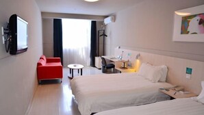 A hotel room with two beds, a red armchair, a desk, a TV, and a window with curtains.