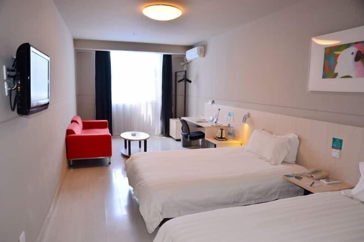 Ett hotellrum med två sängar, en röd fåtölj, ett skrivbord, en tv och ett fönster med gardiner.