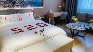 A hotel room with a large bed, a desk, a chair, a sofa, and a small round table with rose petals. - Yongle Star Hotel (Shiyan Fang County) (Fang County)