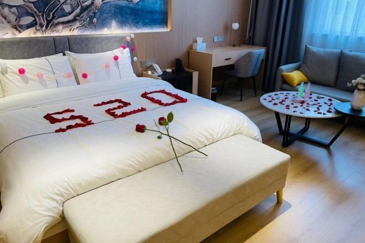 Ett hotellrum med en stor säng, ett skrivbord, en stol, en soffa och ett litet runt bord dekorerat med rosenblad.
