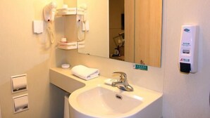 A hotel bathroom with a sink, a mirror, a hairdryer, and a soap dispenser.