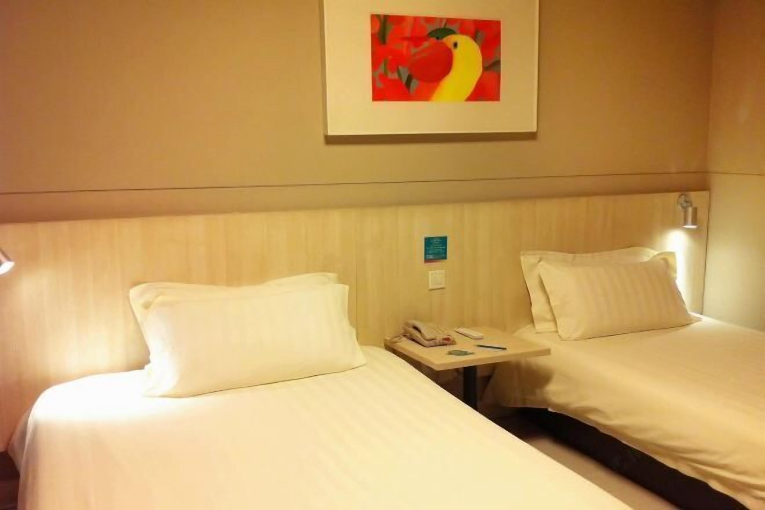 A hotel room with two beds, a small table with a phone and a lamp, and a framed picture on the wall.