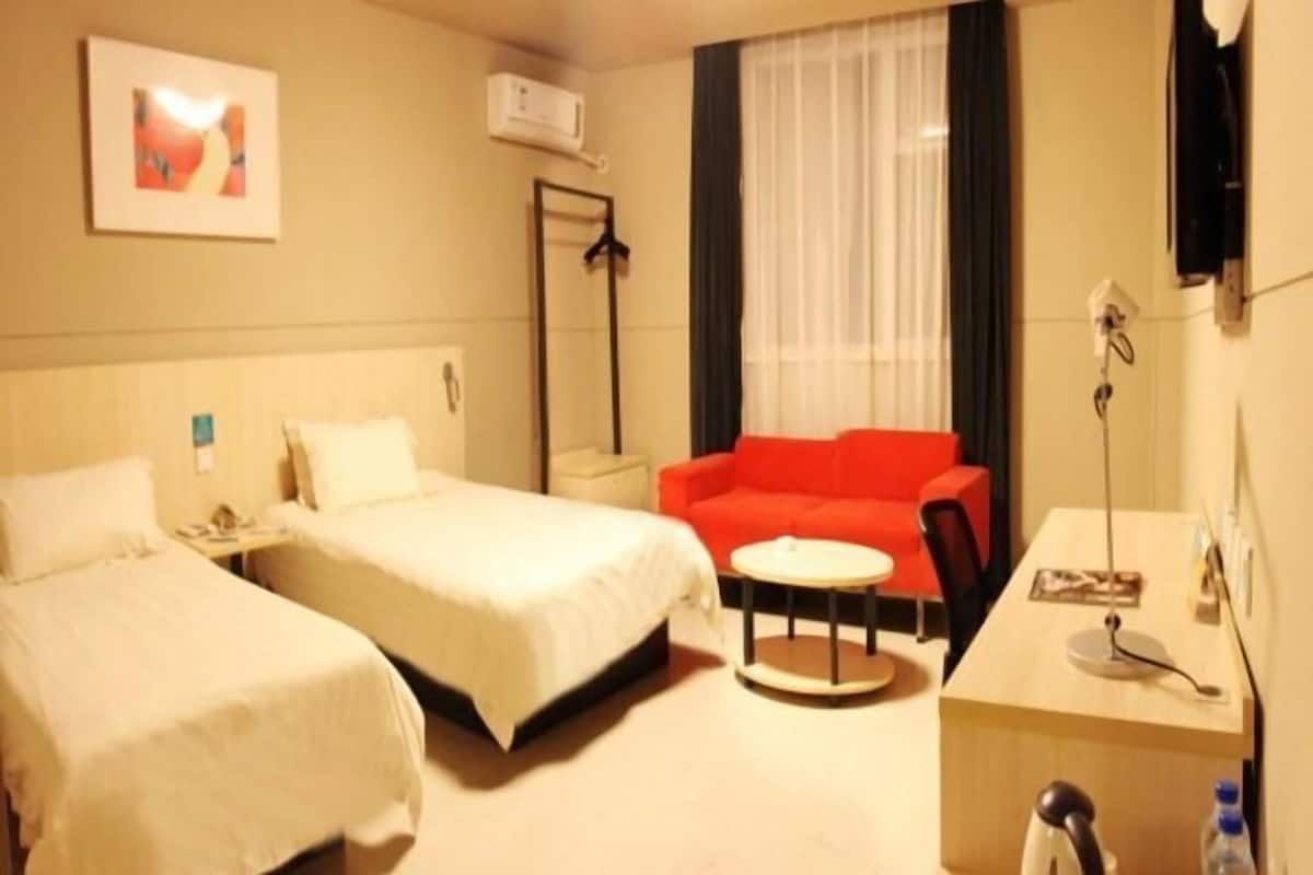 Ett hotellrum med två sängar, en röd soffa, ett skrivbord med en stol och ett fönster med gardiner.