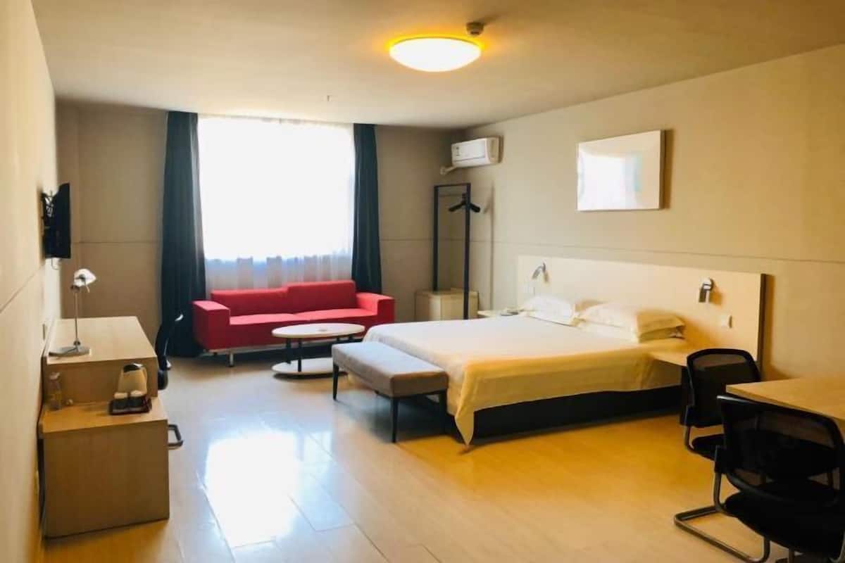 Ett hotellrum med en säng, en röd soffa, ett skrivbord och en stol.
