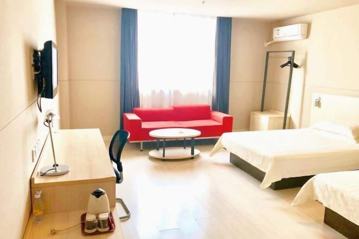 Ett hotellrum med en säng, ett skrivbord, en röd soffa, ett litet runt bord och en garderob.