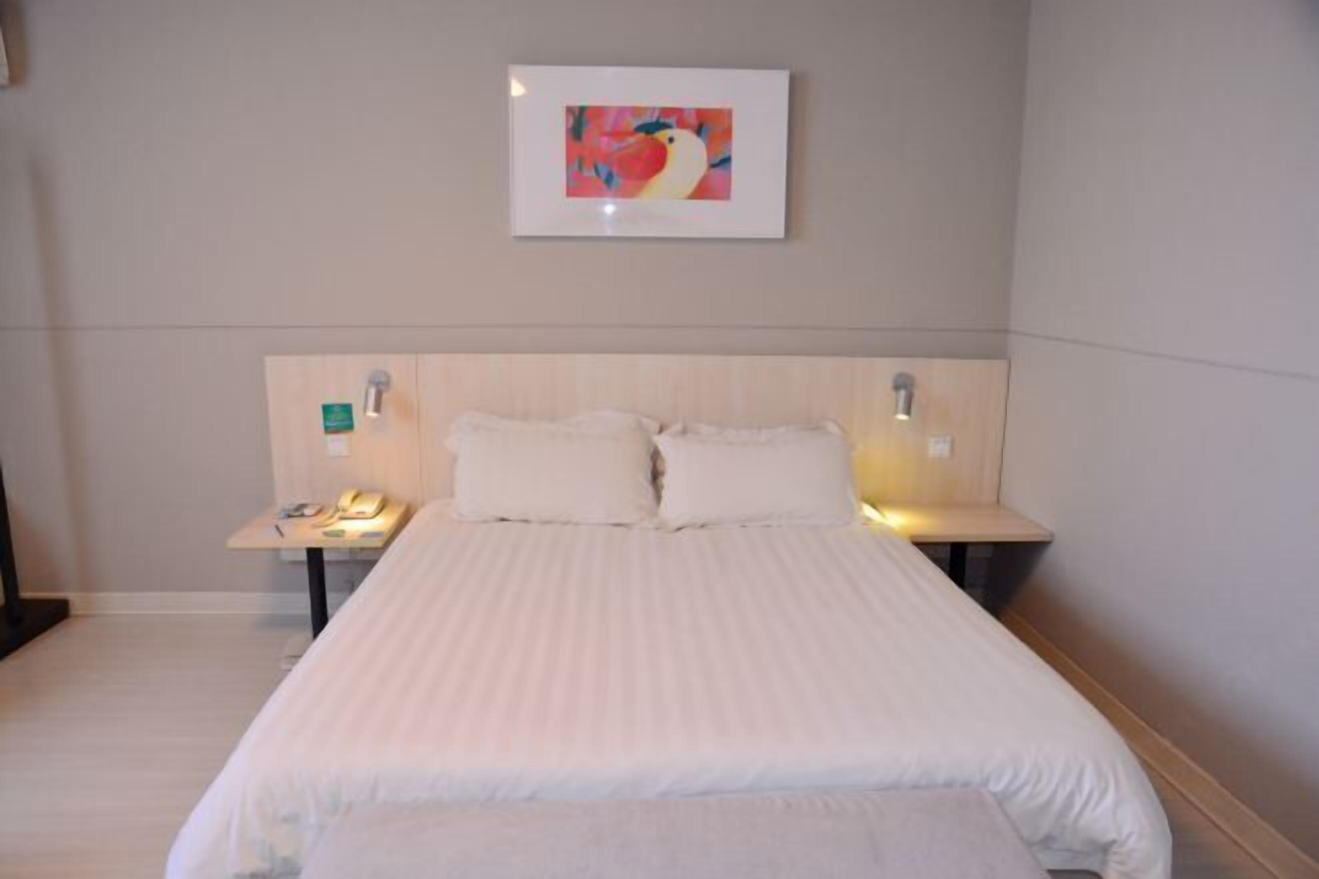 A hotel room with a large bed, two bedside tables, a wall-mounted painting, and a small table with a phone.