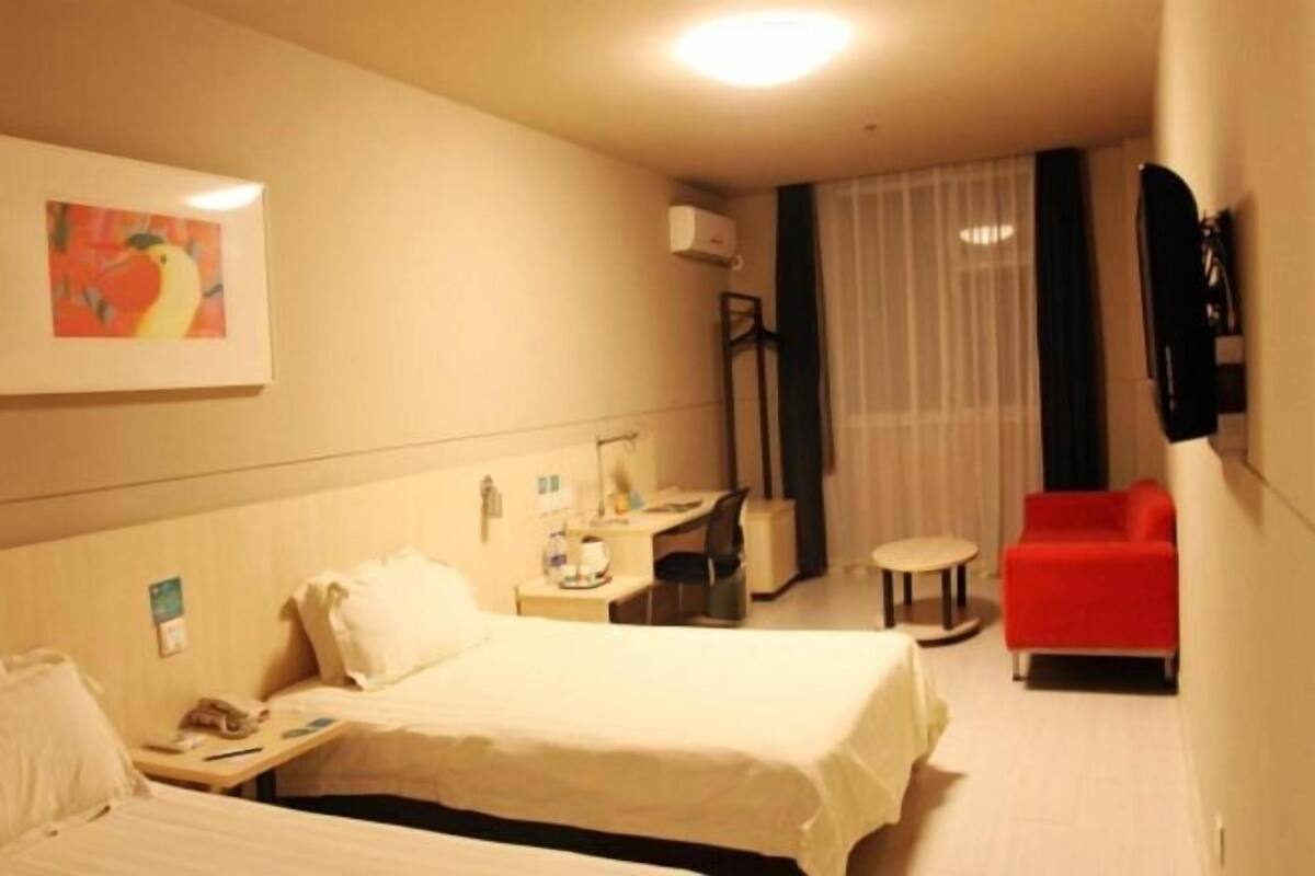 Ett hotellrum med en säng, ett skrivbord med en stol, ett litet bord, en röd fåtölj och en tavla på väggen.