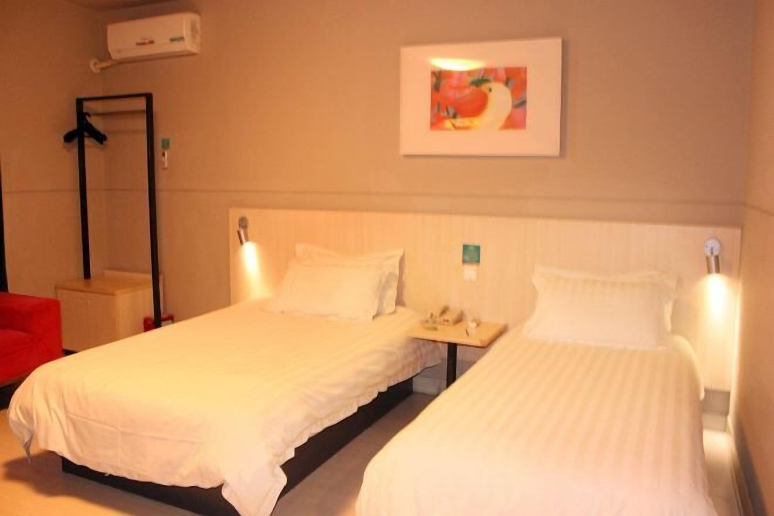 Een hotelkamer met twee bedden, een rode stoel, een spiegel en een schilderij aan de muur.