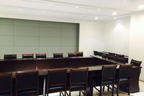 Un salón de conferencias con una larga mesa y sillas, una pared de acento verde e iluminación empotrada en el techo.