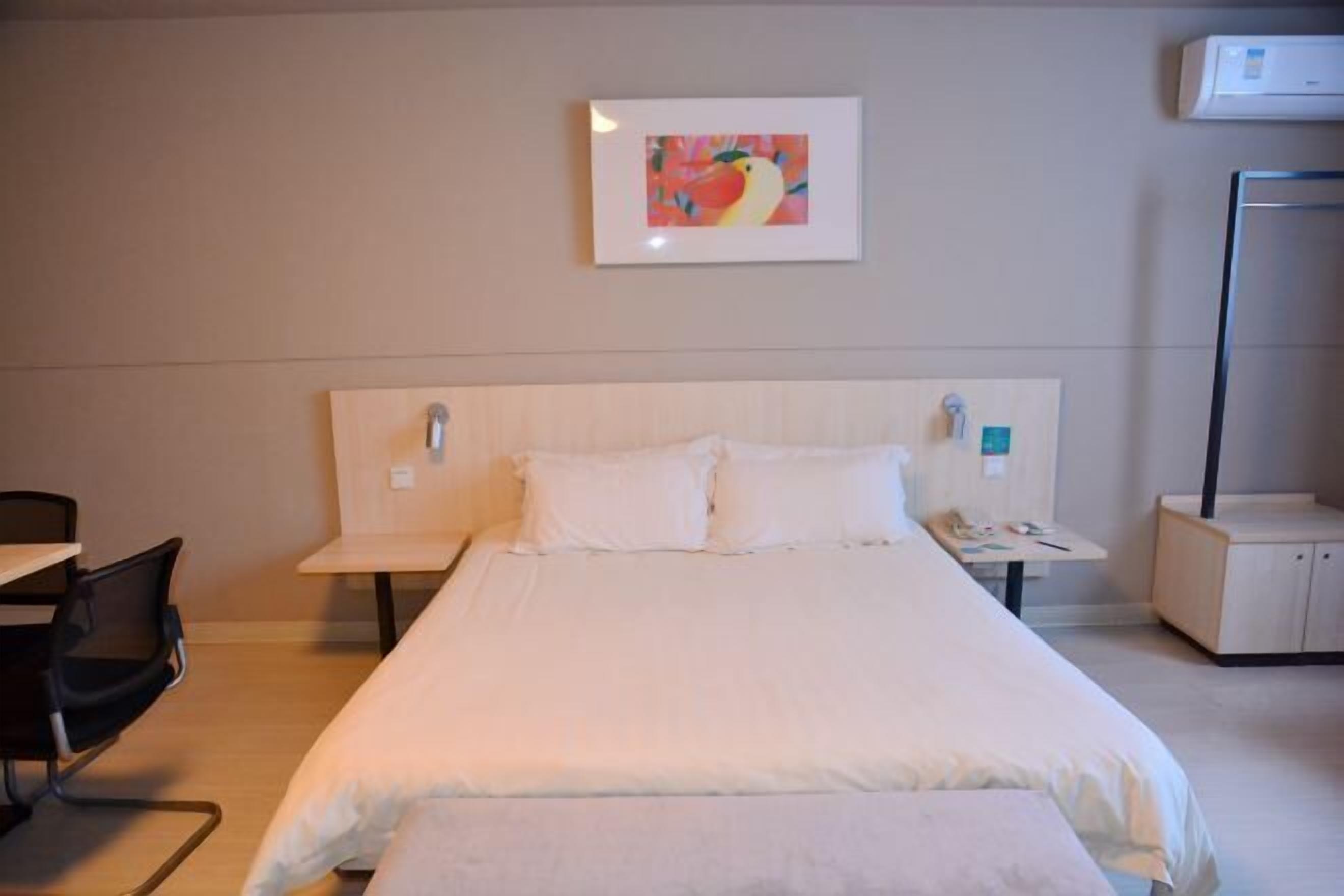 Une chambre d’hôtel comprenant un lit, un bureau, une chaise, une table de chevet, un téléphone et une œuvre d’art accrochée au mur.