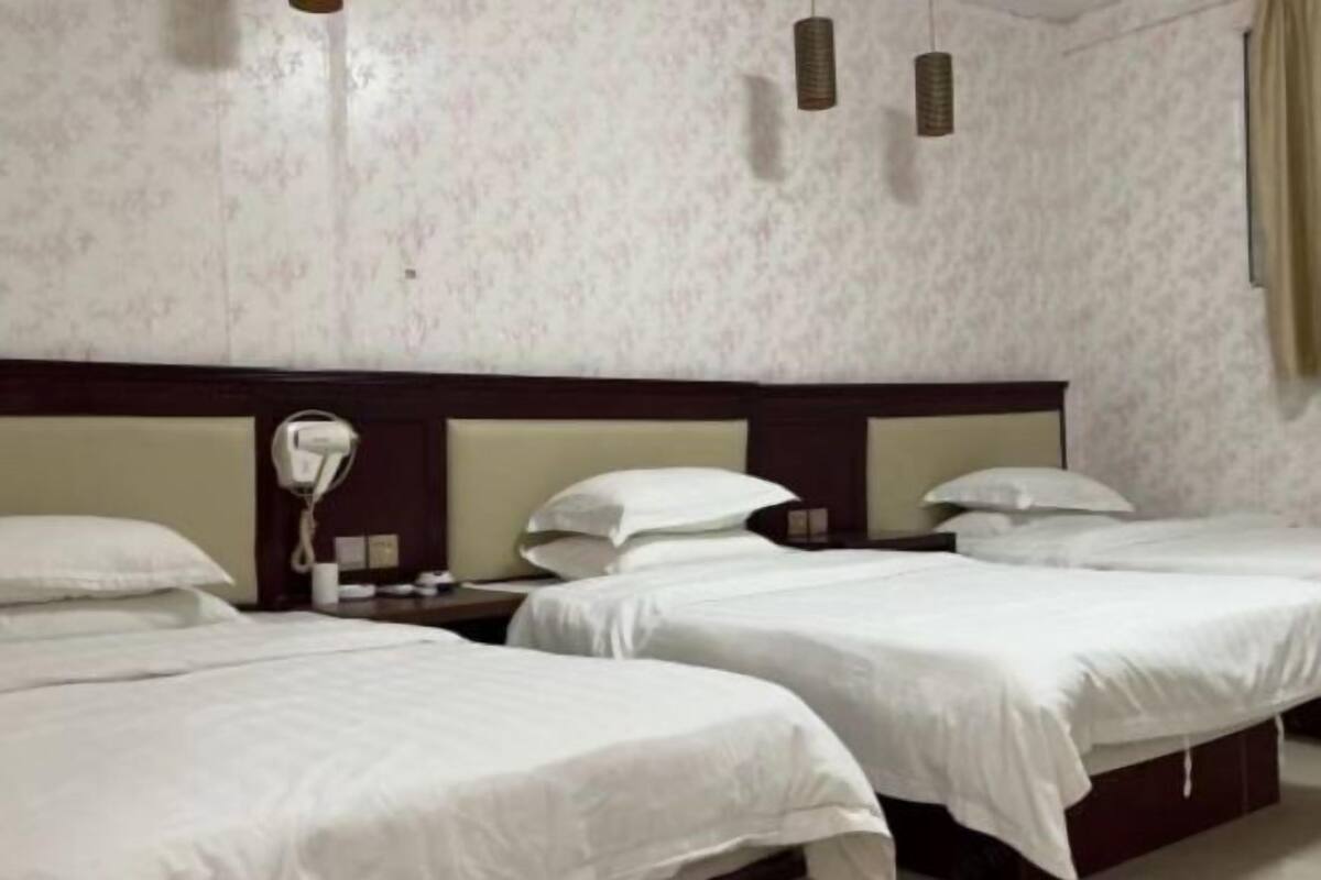 Une chambre d’hôtel avec deux lits, une tête de lit en bois, un téléphone sur la table de chevet et un luminaire fixé au mur.