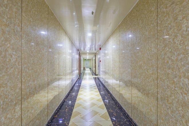 A long, narrow hallway with marble walls and a patterned floor, leading to a door at the end.