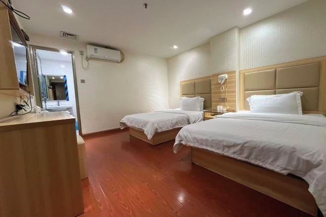 Habitación de hotel con dos camas, un escritorio de madera, un espejo y un equipo de aire acondicionado.