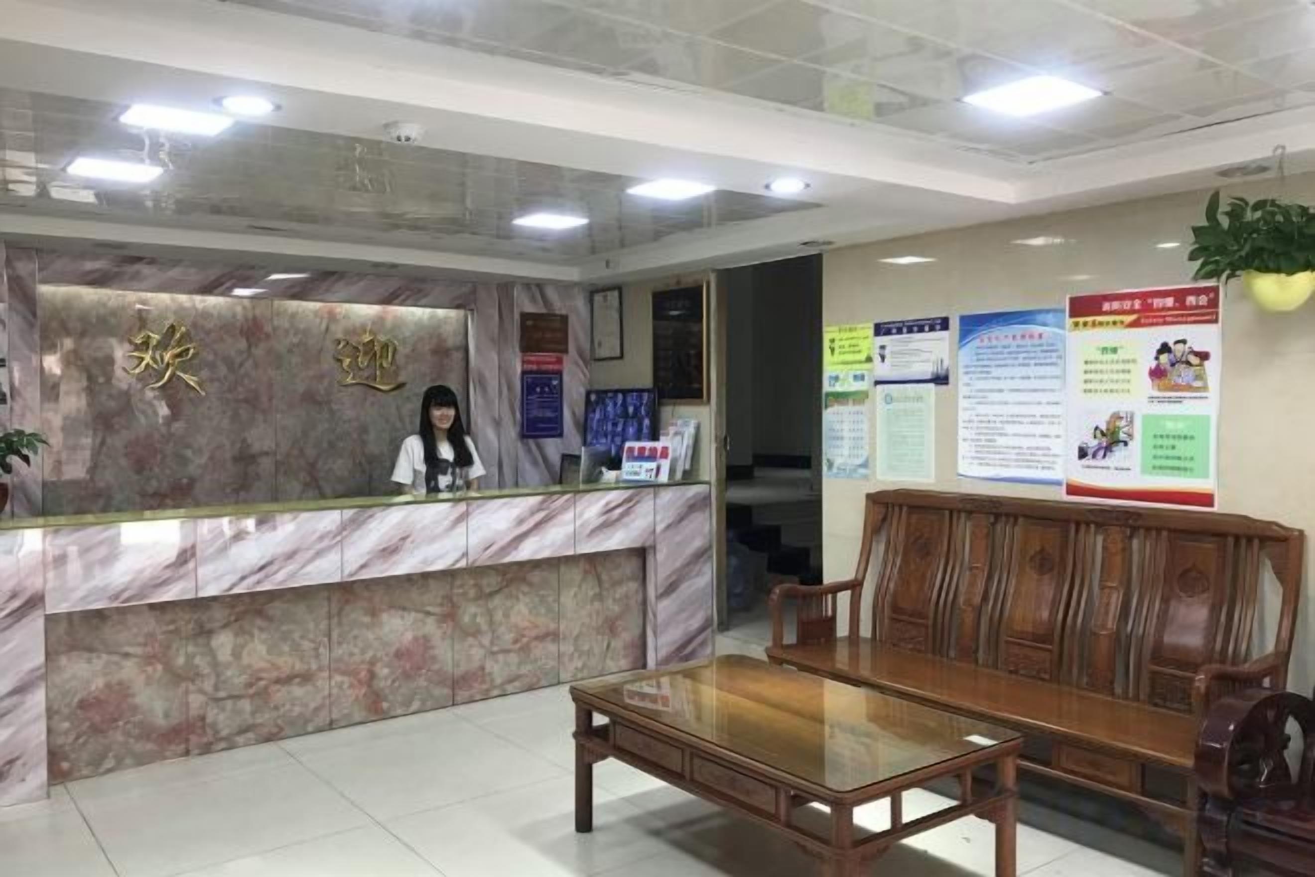 A reception area with a marble counter, a receptionist, a wooden bench, and informational posters on the wall.