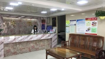 A reception area with a marble counter, a receptionist, a wooden bench, and informational posters on the wall.