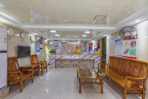 A hotel lobby with a reception desk, wooden seating, a television, and a fan. - Guangzhou Business Hotel (Shangxiajiu Pedestrian Street Changshou Road Subway Station Branch) (Guangzhou)