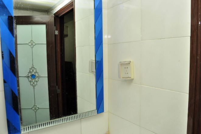 Un baño con paredes de azulejos blancos, un espejo con marco decorativo y una puerta de madera.