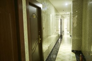A hotel corridor with a wooden door, marble walls, and a checkered floor. - Guangzhou Business Hotel (Shangxiajiu Pedestrian Street Changshou Road Subway Station Branch) (Guangzhou)