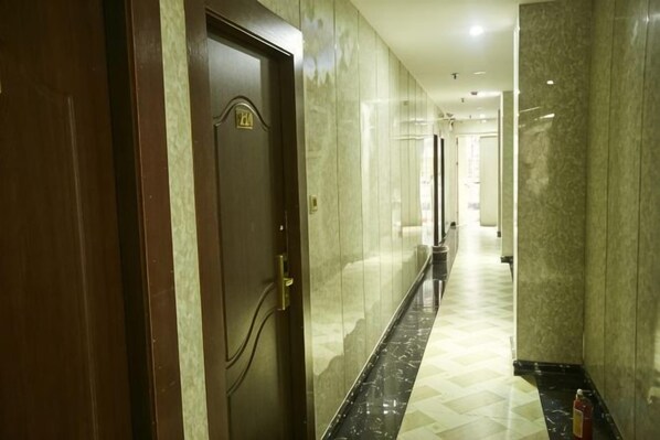 A hotel corridor with a wooden door, marble walls, and a checkered floor.