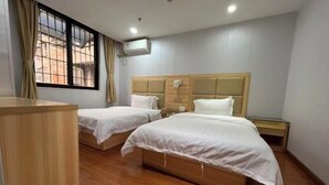 Une chambre d’hôtel avec deux lits, un bureau en bois, une fenêtre avec des rideaux et un appareil de climatisation.
