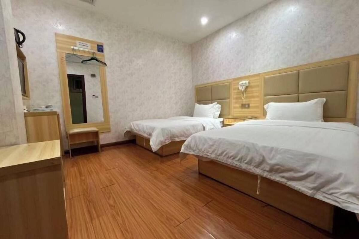 Une chambre d’hôtel avec deux lits, un plancher en bois, un miroir, une table de chevet et un téléphone fixé au mur.